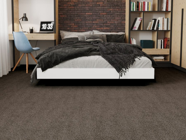 bedroom with a dark upholstered bed and gray bedding, a brick accent wall, a blue chair, and built-in wood shelves with books and decor; gray carpet covers the floor.